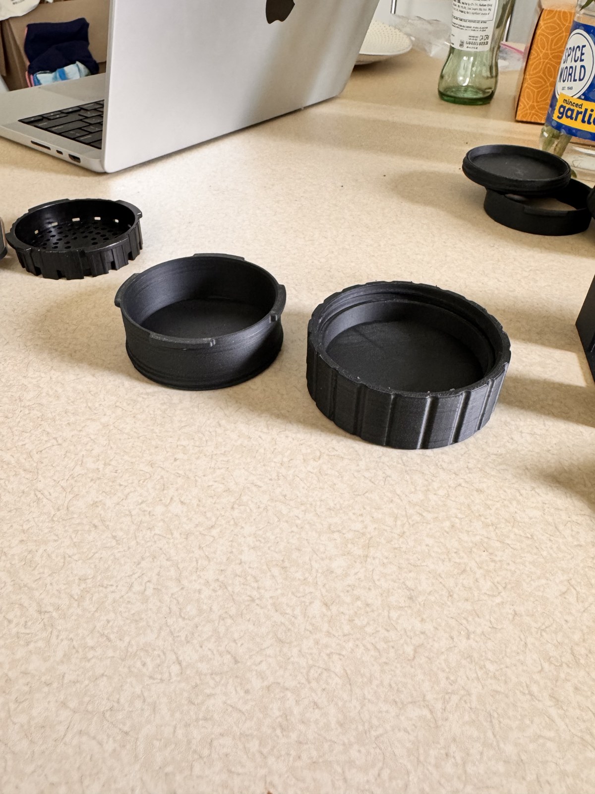 The two halves of the printed filter container set out next to the original AeroPress filter holder for scale, with the AeroPress itself partially visible in the background