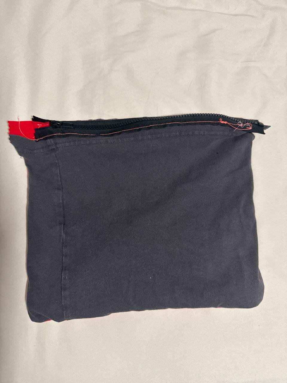 Front view of the finished t-shirt prototype 2 showing the dark grey panel in landscape orientation with the closed black zipper running along the long top edge and visible orange topstitching