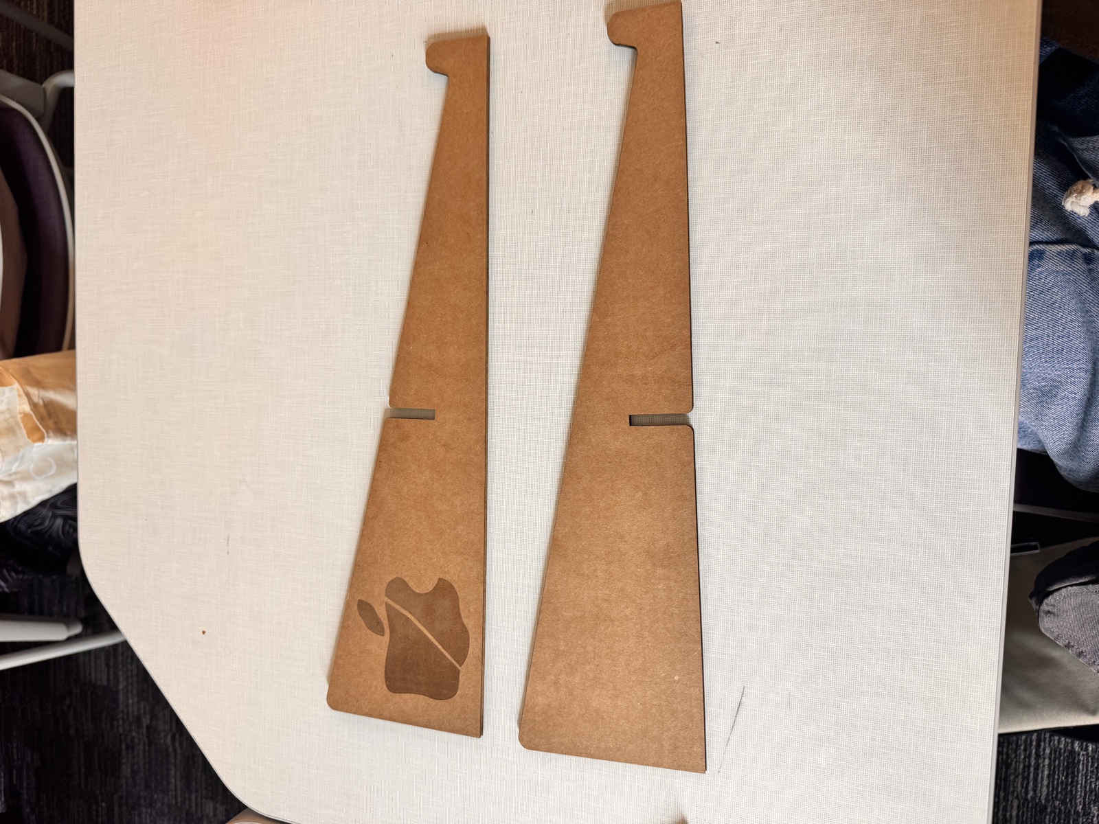 The two finished flute board side panels of the laptop stand laid flat side by side on a white surface, each panel a tall mirrored wedge with a small notched cutout near the upper inside edge for the slot joint, and the left panel showing the engraved wax apple symbol lower on the face