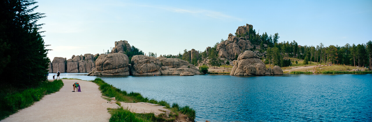 A panoramic view across a lake toward rocky outcrops, with a path along the shore.