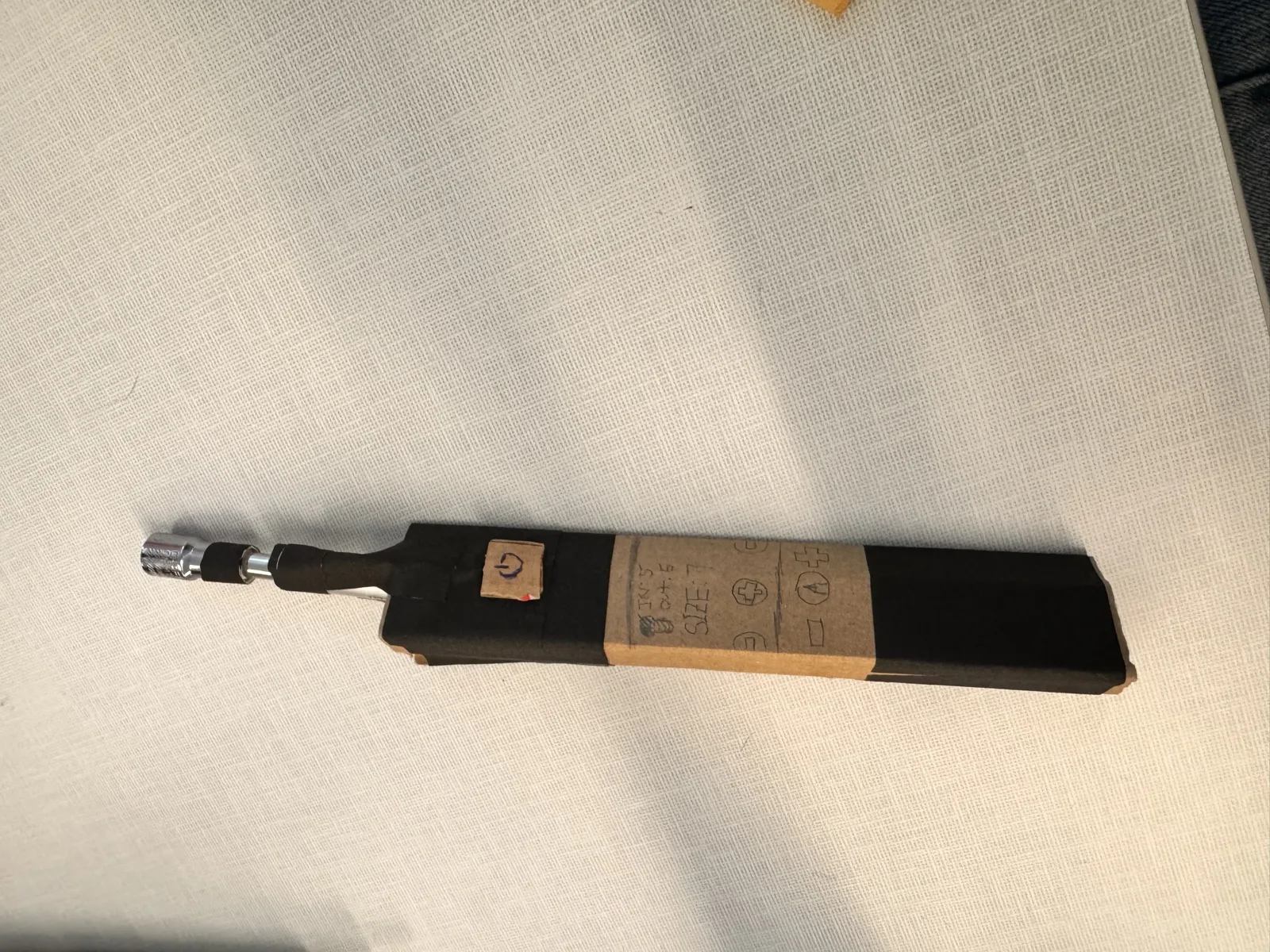 Overhead view of the assembled cardboard prototype showing the full screwdriver with triangular handle wrapped in black tape, pen shaft, and socket head chuck
