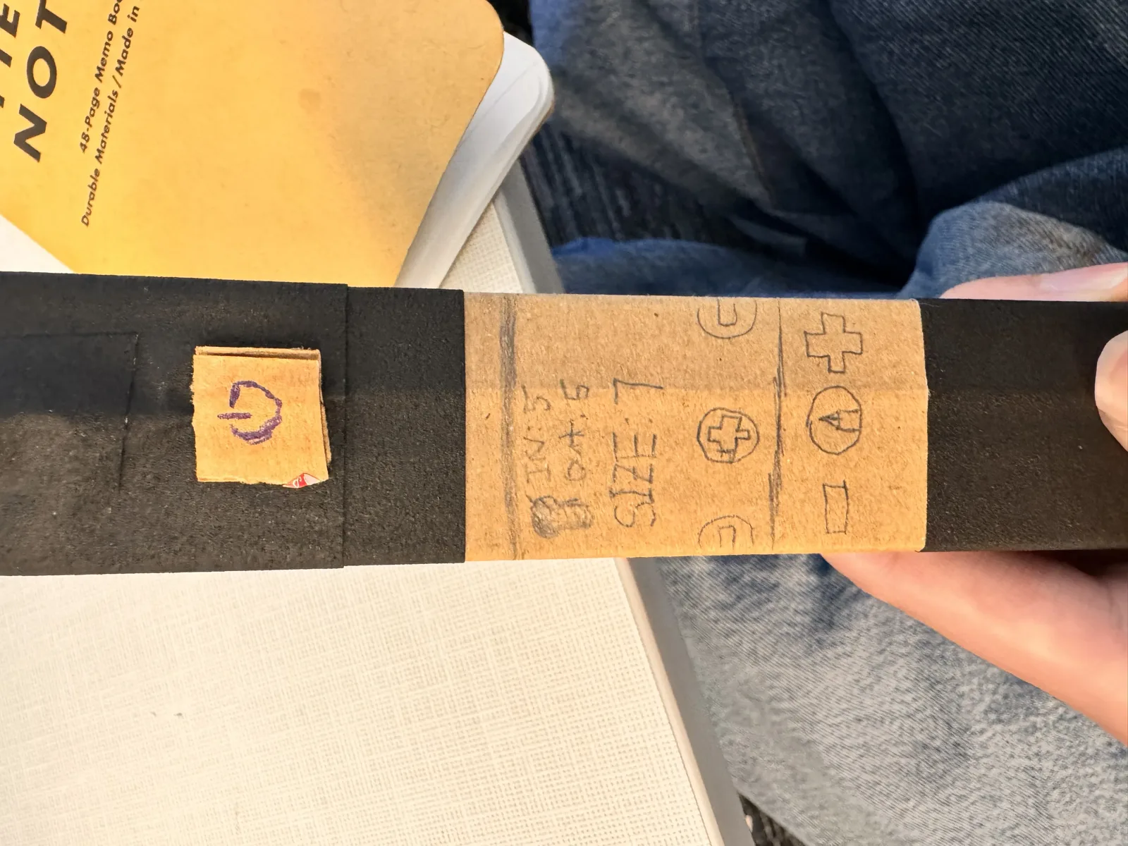 Close-up of the prototype held in hand showing the hand-drawn LCD screen, plus and minus buttons, power button, and bit toggle on the cardboard side panel